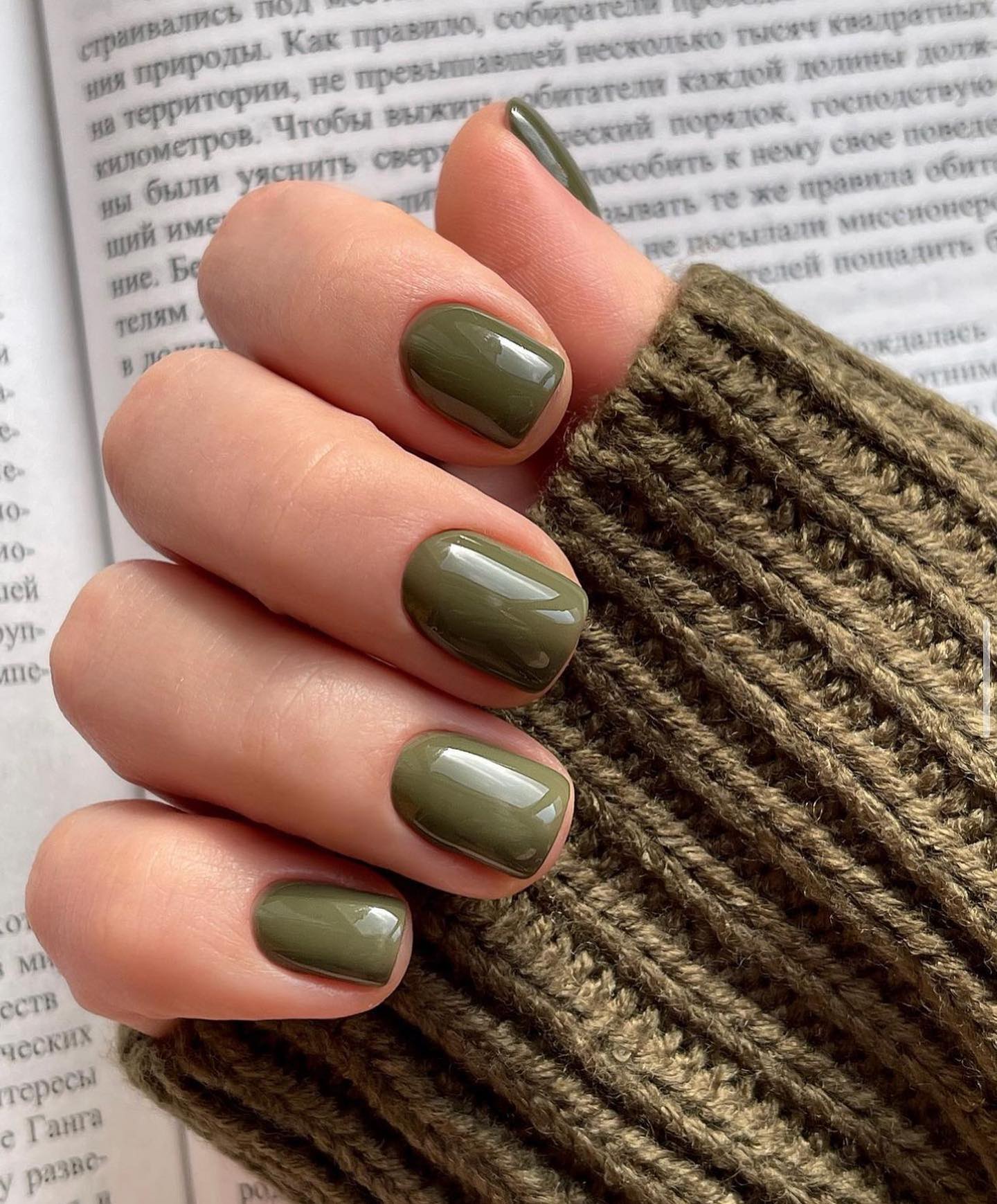 Olive green nails against a knitted sleeve