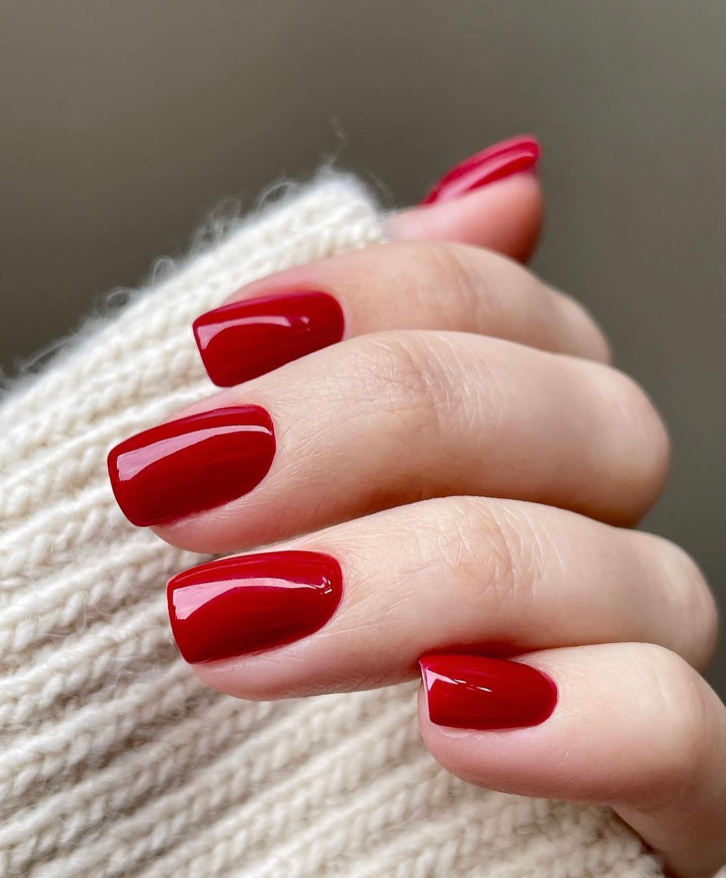 Glossy classic red nails against a cream knit sleeve