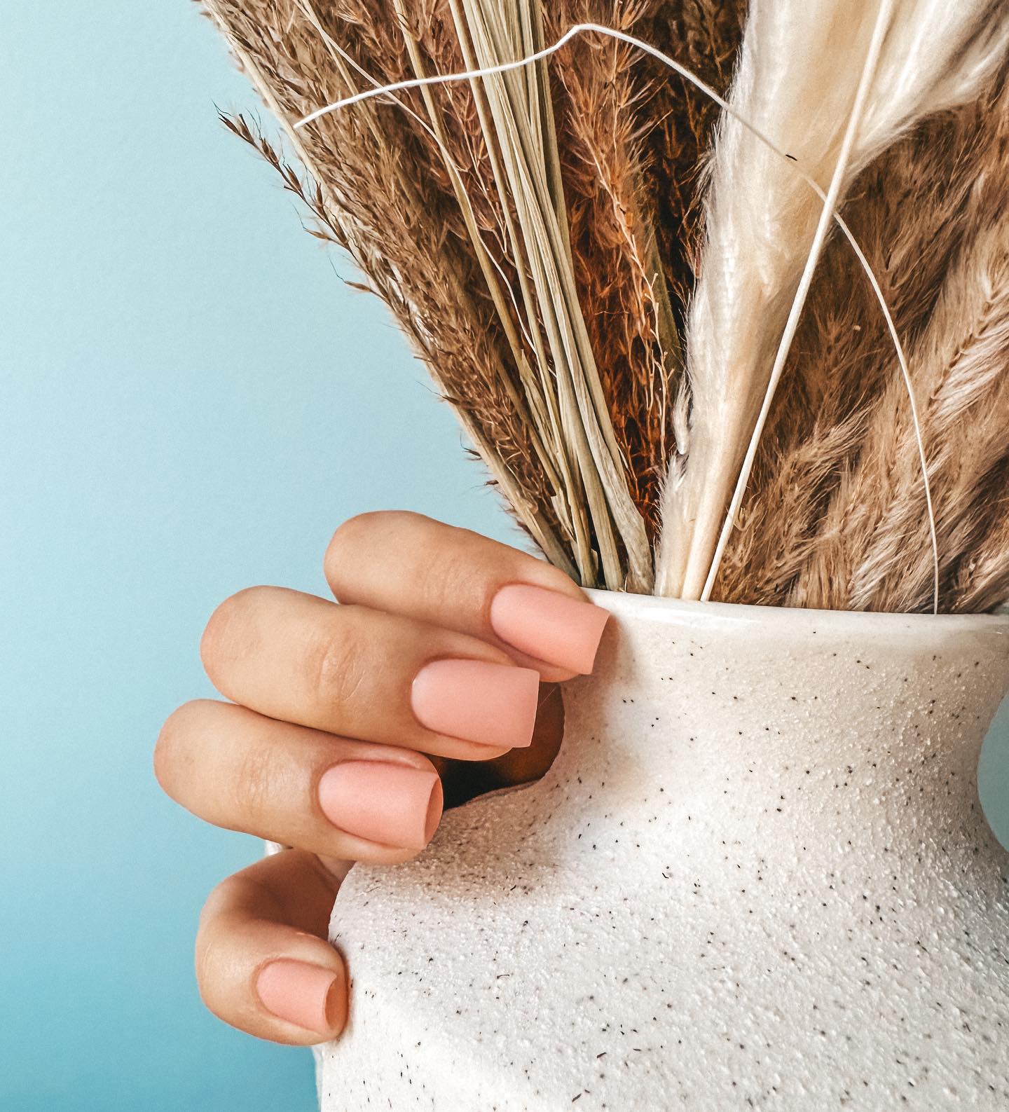 Peach nails holding a vase of dried pampas