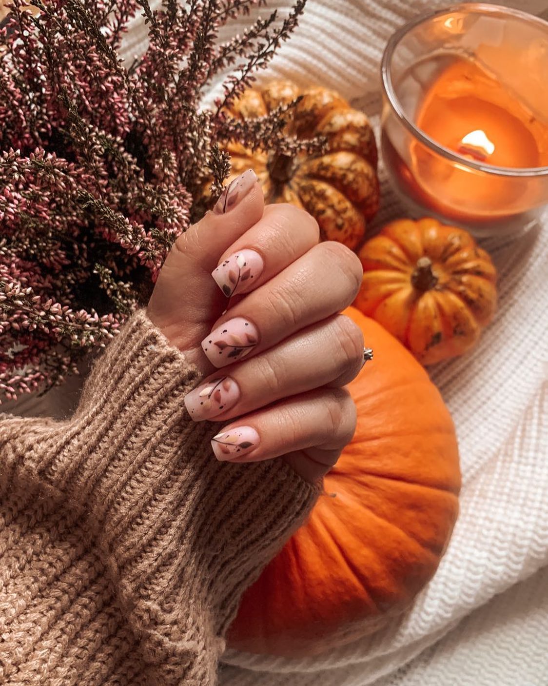 Autumn-inspired nail art beside pumpkins and a candle