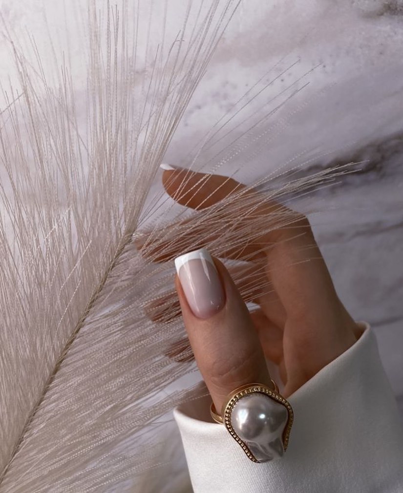 Pearl-white nails beside a feather and pearl ring